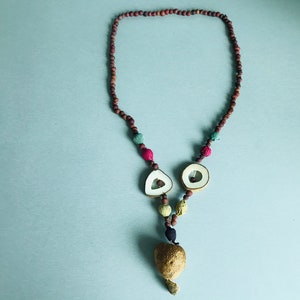 May include: A brown, red, and green beaded necklace with a wooden pendant shaped like a heart. The pendant is made of two halves of a seed pod.