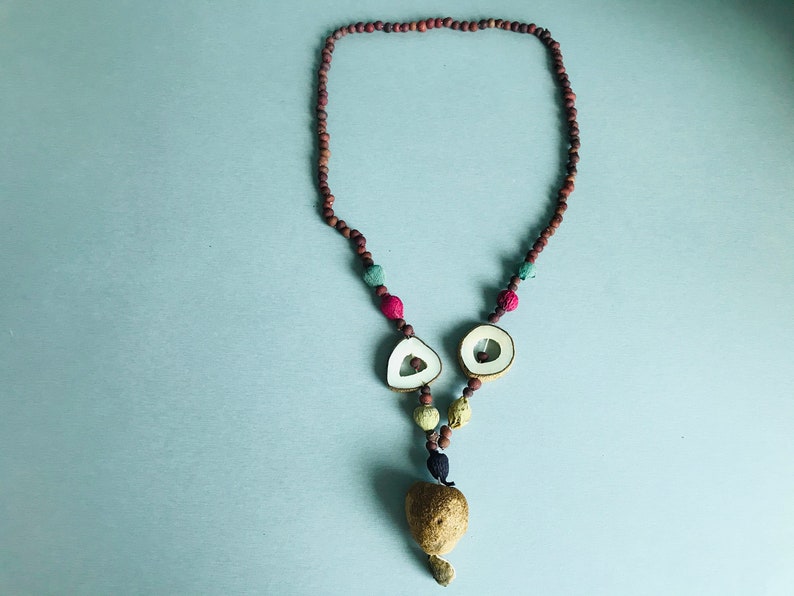 May include: A brown, red, and green beaded necklace with a wooden pendant shaped like a heart. The pendant is made of two halves of a seed pod.
