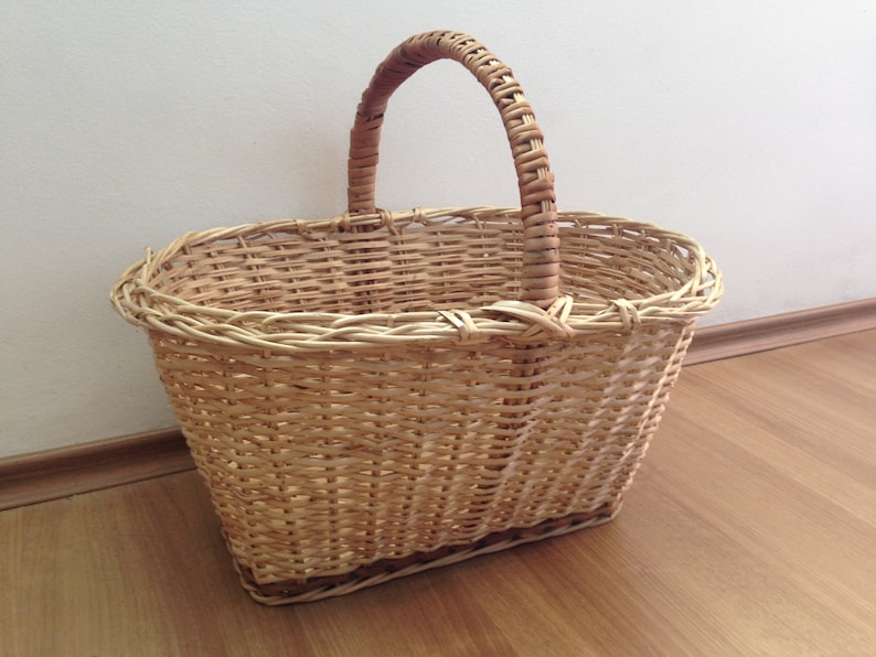 May include: A woven wicker basket with a single handle. The basket is oval shaped and has a light brown color.