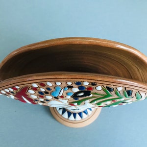 Pode incluir: Um porta-guardanapos de cer&acirc;mica com um design floral em tons de vermelho, azul, verde e branco. O porta-guardanapos tem uma base castanha e uma borda branca.
