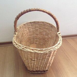 May include: A woven wicker basket with a brown handle. The basket is oval shaped and has a wide opening.