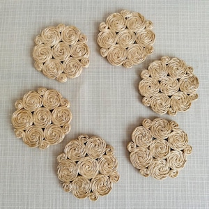 May include: Six round woven coasters made of natural straw with a spiral design. The coasters are beige in colour and have a rustic look.