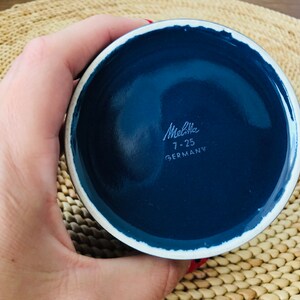 K&ouml;nnte beinhalten: Nahaufnahme des Bodens einer blauen Keramikschale mit wei&szlig;em Rand. Die Schale tr&auml;gt den Aufdruck "Melitta 7-25 DEUTSCHLAND" auf dem Boden.