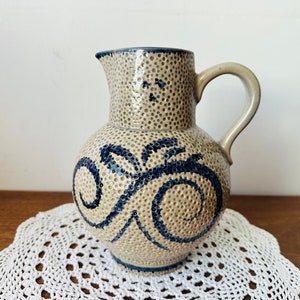 May include: A ceramic jug with a speckled brown glaze and blue floral design. The jug has a round body and a handle.