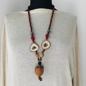 May include: A long necklace made of brown, red, and green beads with two white wooden pendant shapes and a brown wooden pendant at the bottom.