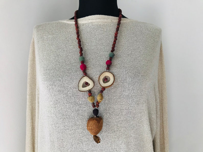 May include: A long necklace made of brown, red, and green beads with two white wooden pendant shapes and a brown wooden pendant at the bottom.