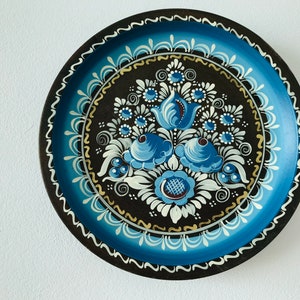 May include: A round wooden plate with a blue and white floral design painted on a black background. The plate has a gold rim and is surrounded by a blue and white border.