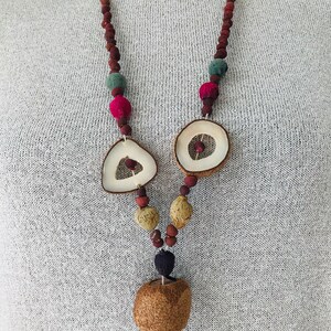 May include: A long necklace made of brown wooden beads, with a variety of natural materials including dried fruit, wood, and seed pods. The necklace features a large, round, dried fruit pendant.