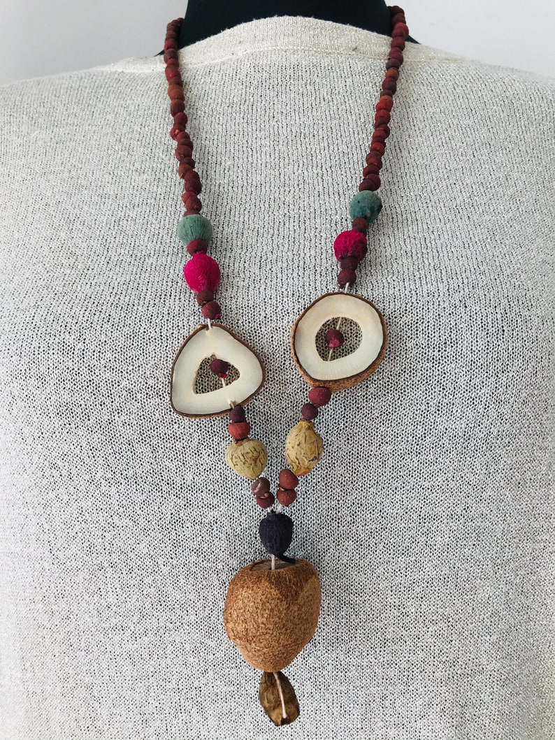 May include: A long necklace made of brown wooden beads, with a variety of natural materials including dried fruit, wood, and seed pods. The necklace features a large, round, dried fruit pendant.