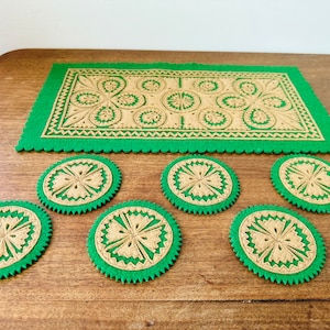 May include: A set of six green and tan felt coasters with a decorative pattern. The coasters are arranged in a circle on a wooden surface.