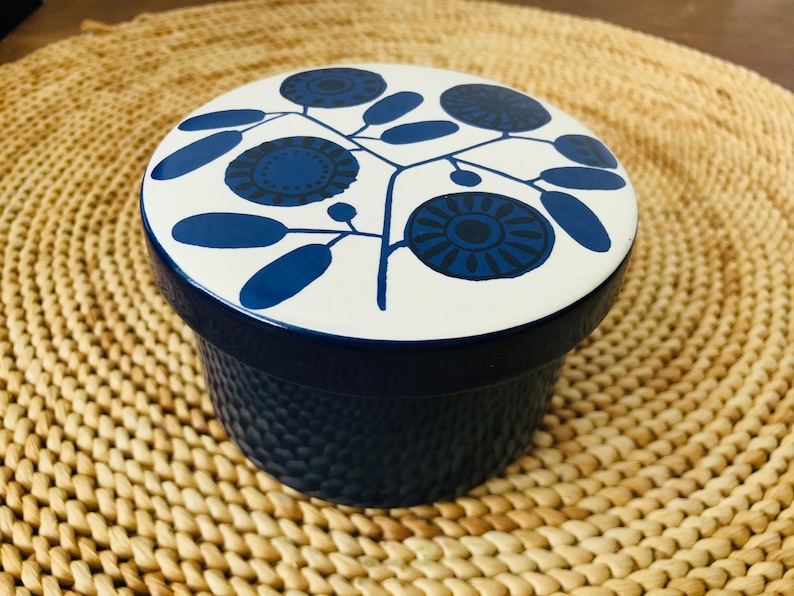 K&ouml;nnte beinhalten: Ein blauer und wei&szlig;er Keramikbeh&auml;lter mit einem Blumendesign. Der Deckel hat einen wei&szlig;en Hintergrund mit blauen Blumen und Bl&auml;ttern. Der Beh&auml;lter ist blau.