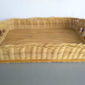 Può includere: Un cesto rettangolare in vimini con fondo in legno e un bordo decorativo con perline. Il cesto è di colore marrone chiaro e presenta un motivo intrecciato.
