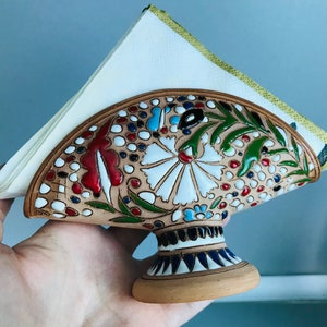 Pode incluir: Porta-guardanapos de cer&acirc;mica com um design floral em tons de vermelho, verde, branco e azul. O porta-guardanapos tem uma parte superior em forma de leque e uma base redonda.