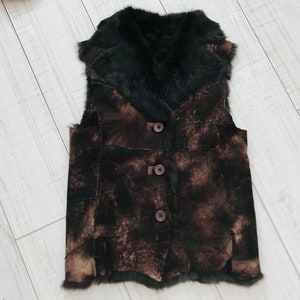 May include: A brown suede vest with a black fur collar and three brown buttons. The vest has a patchwork design.