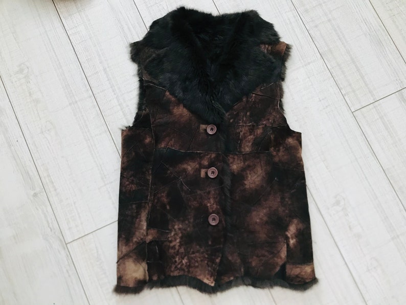 May include: A brown suede vest with a black fur collar and three brown buttons. The vest has a patchwork design.