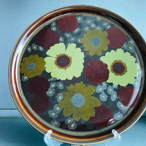 Può includere: Un piatto da portata in ceramica marrone con un motivo floreale. I fiori sono in tonalità di giallo, verde e rosso.