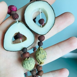 May include: A necklace made of natural materials, including wood, seeds, and berries. The necklace features two large wooden circles with cut-out centers, and a variety of smaller round and oval beads.