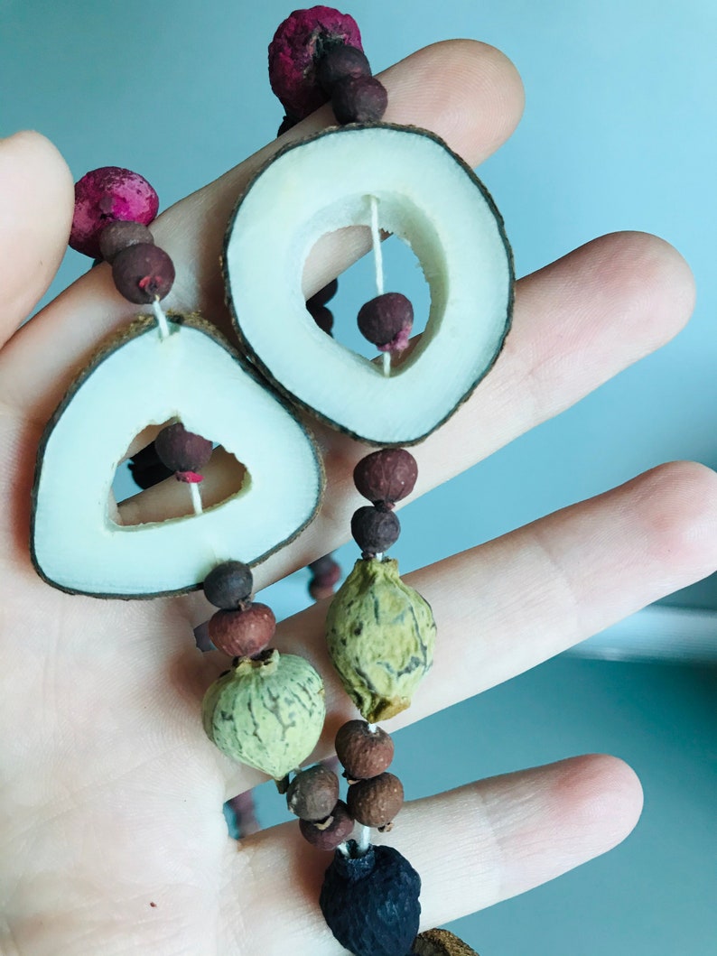 May include: A necklace made of natural materials, including wood, seeds, and berries. The necklace features two large wooden circles with cut-out centers, and a variety of smaller round and oval beads.