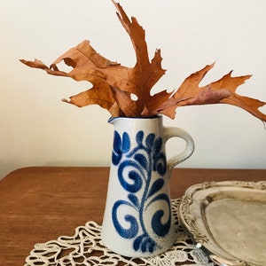 May include: A blue and white ceramic jug with a floral design, filled with dried brown leaves.