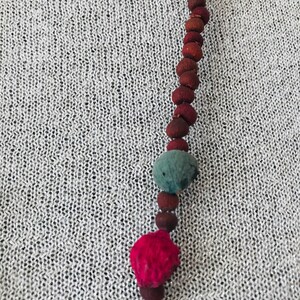 May include: A long necklace made of brown, red, and blue beads. The beads are round and have a natural, rustic look.