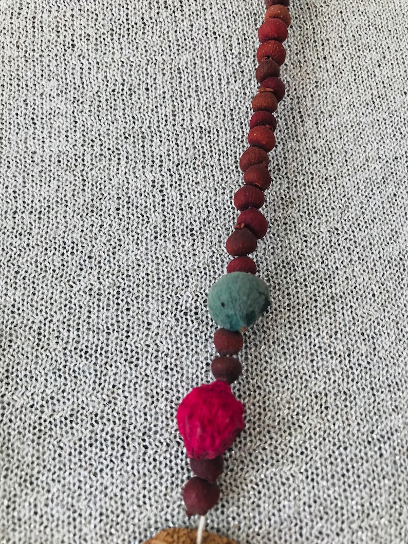 May include: A long necklace made of brown, red, and blue beads. The beads are round and have a natural, rustic look.