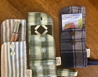 May include: Three handmade fabric pouches made from repurposed shirt sleeves. The pouches are in striped, plaid, and solid patterns. One pouch holds a tube of makeup. The other two hold a gift card and a card with the text "Udderly Country Gifts Handmade For You".