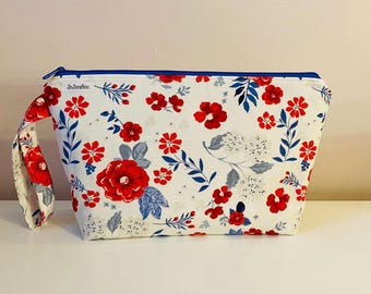 May include: A white zippered pouch with a blue zipper and a blue trim. The pouch has a red and white floral pattern with the text "JnJeraftoo" printed on the front.