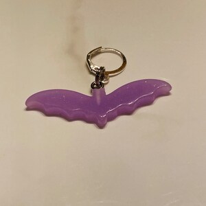 May include: A purple glitter bat charm with a silver hoop earring attached.