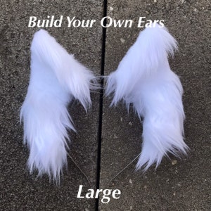 May include: A pair of large, white, fluffy faux fur ears for cosplay or costume making. The ears are attached to a headband. The text "Build Your Own Ears" and "Large" are visible in the image.
