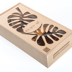 Puede incluir: Una caja rectangular de madera con un diseño de hoja de monstera cortada con láser en la tapa. La caja tiene la palabra "cupré" en la tapa y "Colombia" en el lateral. La caja es de madera clara.