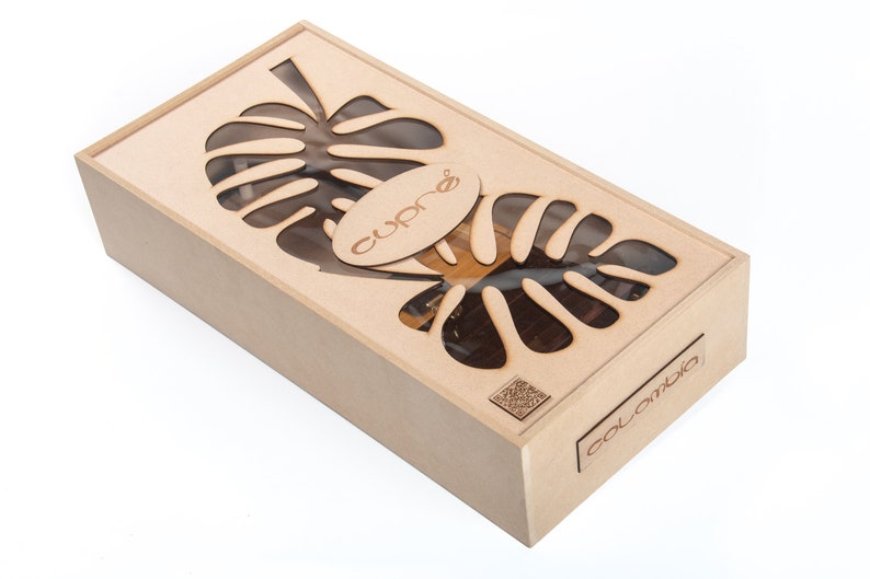 May include: A rectangular wooden box with a laser-cut monstera leaf design on the lid. The box has the word "cupr&eacute;" on the lid and "Colombia" on the side. The box is made of light-coloured wood.