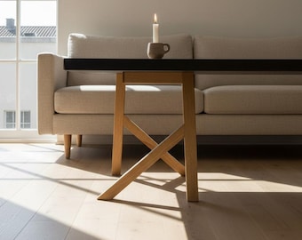 May include: A modern living room scene featuring a light-colored sofa, a black-topped table with a unique wooden base, and a lit candle in a small mug. The room has hardwood floors and a large window.
