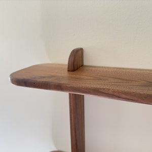 K&ouml;nnte beinhalten: Ein Holzregal mit abgerundeter Kante und schlichtem Design. Das Regal ist aus dunklem Holz mit nat&uuml;rlicher Oberfl&auml;che.