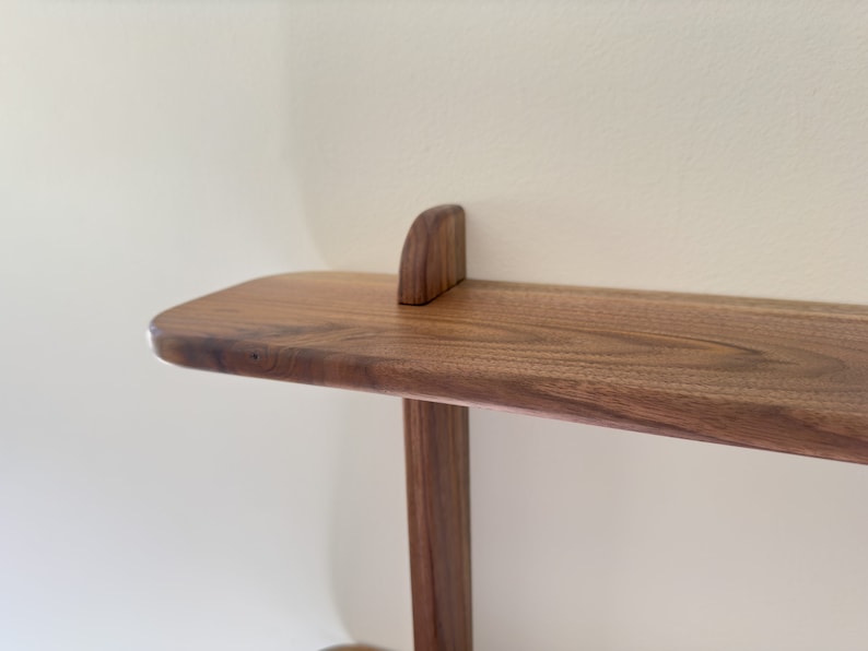 K&ouml;nnte beinhalten: Ein Holzregal mit abgerundeter Kante und schlichtem Design. Das Regal ist aus dunklem Holz mit nat&uuml;rlicher Oberfl&auml;che.