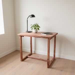 May include: A small, rustic wooden table with a natural finish. A black desk lamp, a small potted plant, and a notebook rest on the tabletop. The table is 24 inches wide, 18 inches deep, and 28 inches tall.