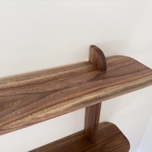 K&ouml;nnte beinhalten: Ein zweistufiges Holzregal mit abgerundeter Kante. Das Regal ist aus Walnussholz gefertigt und hat eine nat&uuml;rliche Oberfl&auml;che.