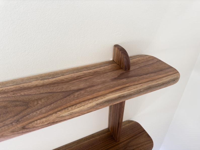 K&ouml;nnte beinhalten: Ein zweistufiges Holzregal mit abgerundeter Kante. Das Regal ist aus Walnussholz gefertigt und hat eine nat&uuml;rliche Oberfl&auml;che.