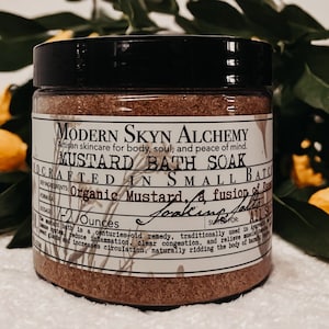 Pode incluir: Um frasco de vidro castanho com tampa preta cheio de um banho de imersão castanho. O rótulo diz "Modern Skyn Alchemy Mustard Bath Soak Crafted in Small Batches Organic Mustard. A fusion of Essential Oils. Suitable for: All Skin Types. 2 Ounces. O banho de mostarda é um remédio ancestral, tradicionalmente usado na Ayurveda para desintoxicar o sistema linfático, reduzir a inflamação, limpar a congestão e aliviar a tensão muscular. Também aumenta a circulação, eliminando naturalmente as toxinas nocivas do corpo."