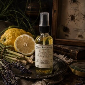 May include: A clear glass spray bottle of Modern Skyn Alchemy Bug Bite Anti-Itch Oil with a black pump top. The label features the text Modern Skyn Alchemy, Bug Bite Anti-Itch Oil, and 59 ml. The bottle contains a golden liquid with visible botanicals.