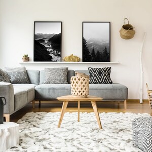 May include: A gray sectional sofa with black and white patterned throw pillows in a living room with a fireplace, a coffee table, and a rug. Two black and white framed landscape photos are on the wall above the sofa.