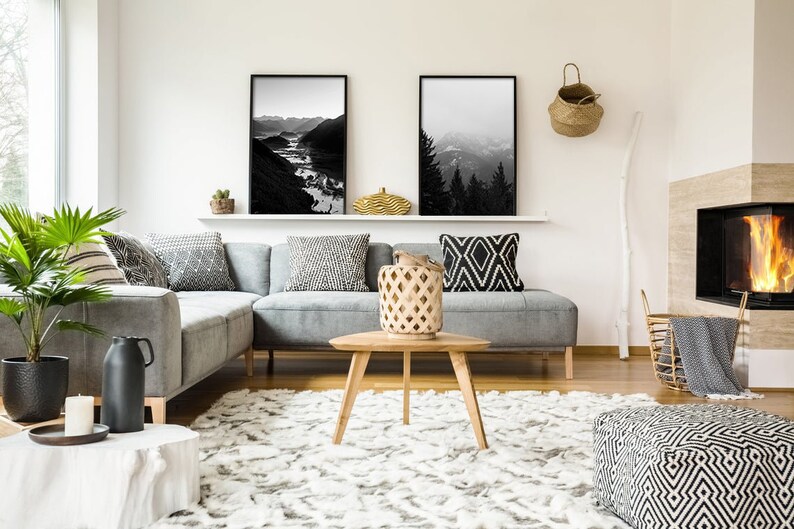 May include: A gray sectional sofa with black and white patterned throw pillows in a living room with a fireplace, a coffee table, and a rug. Two black and white framed landscape photos are on the wall above the sofa.