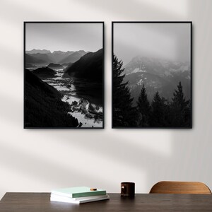 May include: Two black and white framed photographs of mountain landscapes. The left photo shows a valley with a river winding through it. The right photo shows a mountain range with trees in the foreground.