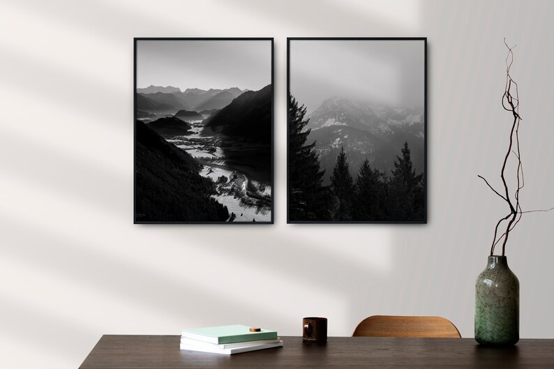 May include: Two black and white framed photographs of mountain landscapes. The left photo shows a valley with a river winding through it. The right photo shows a mountain range with trees in the foreground.