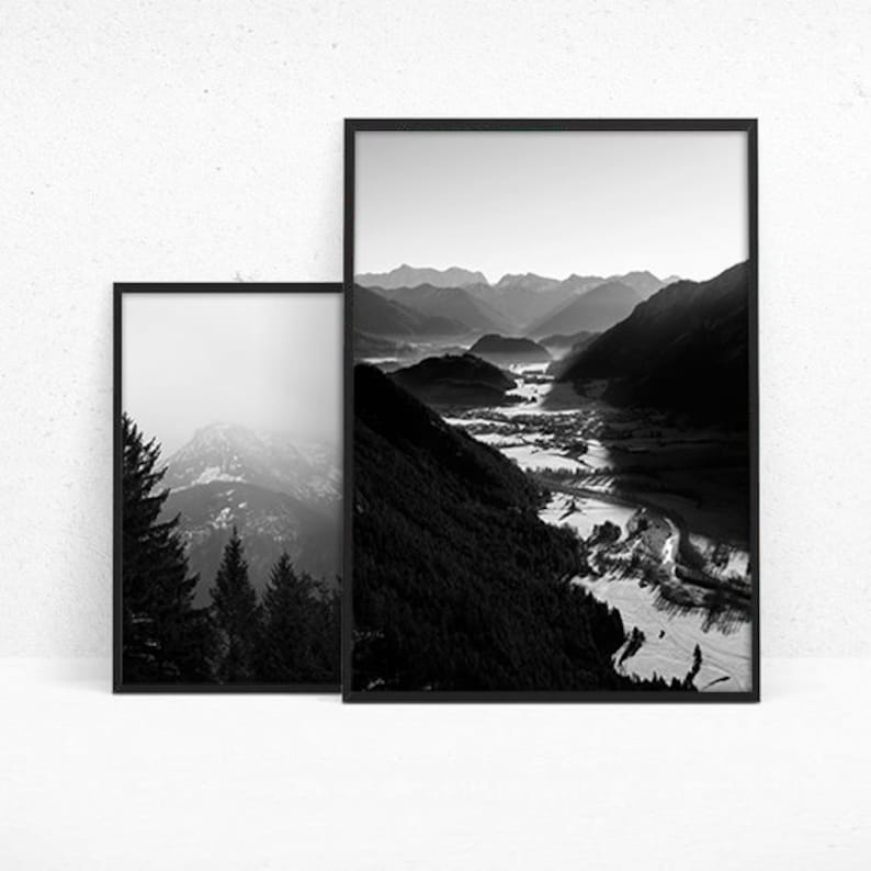 May include: Black and white photograph of a mountain range with a valley in the foreground. The mountains are covered in trees and the valley is filled with a river.