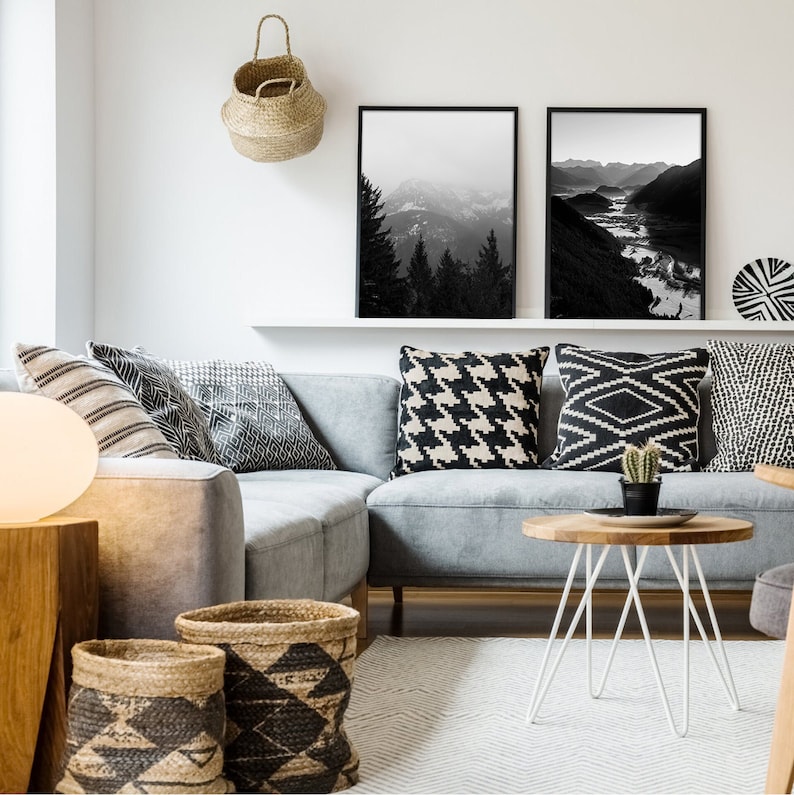 May include: A gray sectional sofa with black and white patterned throw pillows. The sofa is in a living room with a white coffee table and a woven basket hanging on the wall. Two black and white framed landscape photos are hanging above the sofa.
