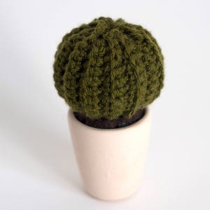 Peut inclure: Un petit cactus en tricot vert dans un pot en céramique blanc.