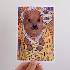 Puede incluir: Una lámina de arte rectangular que muestra un quokka marrón con una túnica decorativa de tono dorado con patrones geométricos complejos, motivos circulares y acentos coloridos. El quokka está centrado, enmarcado por un fondo en forma de halo.