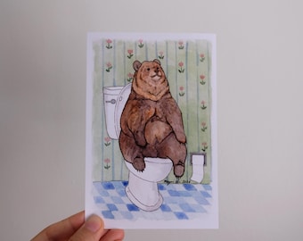 Könnte beinhalten: Eine Aquarellillustration auf einer rechteckigen Karte, die einen braunen Bären auf einer weißen Toilette zeigt. Der Hintergrund besteht aus grüner Tapete mit kleinem rosa Blumenmuster und einem blau-weiß karierten Boden mit Toilettenpapier.