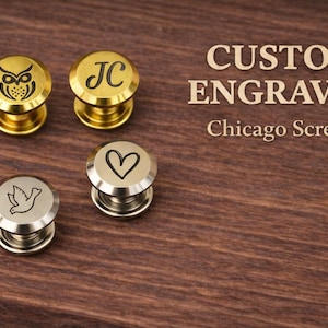 Könnte beinhalten: Vier individuell gravierte Chicago-Schrauben mit verschiedenen Designs: eine Eule, die Initialen "JC", ein Herz und eine Taube. Die Schrauben sind gold- und silberfarben, vor einem dunklen Holzmaserungshintergrund. Der Text "CUSTOM ENGRAVED" ist ebenfalls sichtbar.