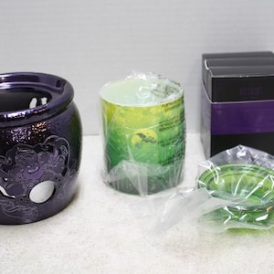 May include: A dark purple ceramic wax warmer featuring a debossed character design, a green cylindrical wax melt insert wrapped in clear plastic, a small green glass dish in plastic packaging, and a black box with a purple band labeled Villains.